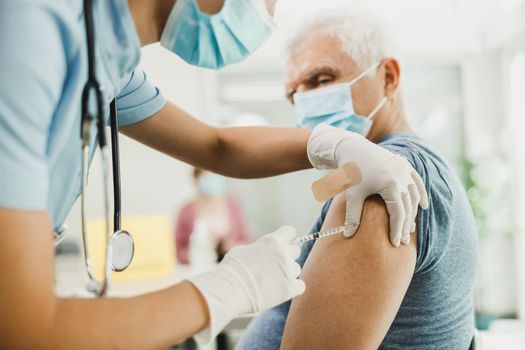 A nurse giving a vaccine to senior man due to coronavirus pandemic.
