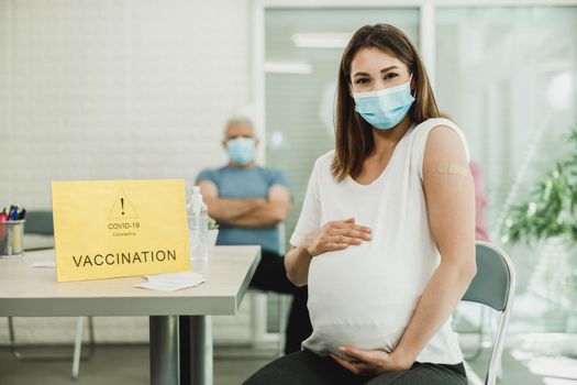 A pregnant woman sitting and holding her belly after receiving a coronavirus vaccine. Looking at camera.