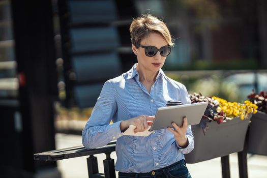 Mature businesswoman is using digital tablet in front of office during break.