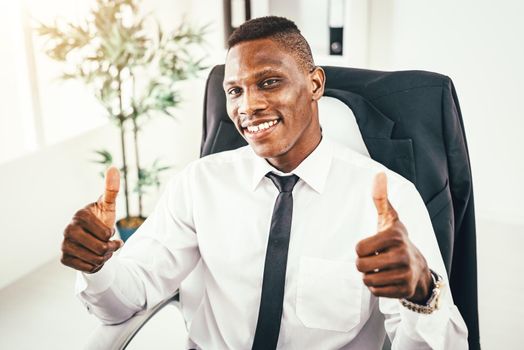 African businessman is sitting in the office, satisfied with success and shows thumbs up.