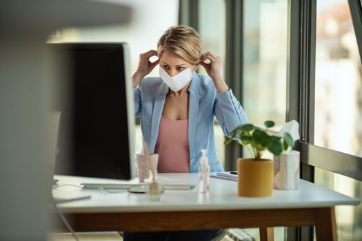 Business woman in a medical protective mask works at the computer during self-isolation and quarantine to avoid infection during flu virus outbreak and coronavirus epidemic.