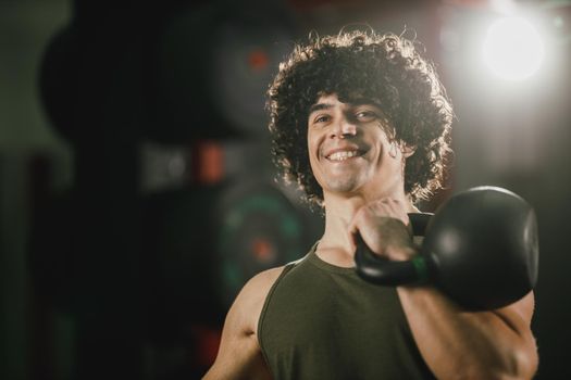A young muscular man is doing hard training with kettlebell at the gym.