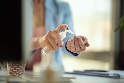 Close-up of a unrecognizable business woman uses antibacterial antiseptic gel for hands disinfection in a works place at the computer during self-isolation and quarantine to avoid infection during flu virus outbreak and coronavirus epidemic .