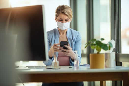 Business woman in a medical protective mask works from home at the computer, using smartphone, during self-isolation and quarantine to avoid infection during flu virus outbreak and coronavirus epidemic.