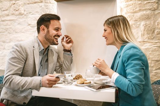 Young man and young woman sitting at cafe and talking with smile. They drinking coffee and having breakfast.