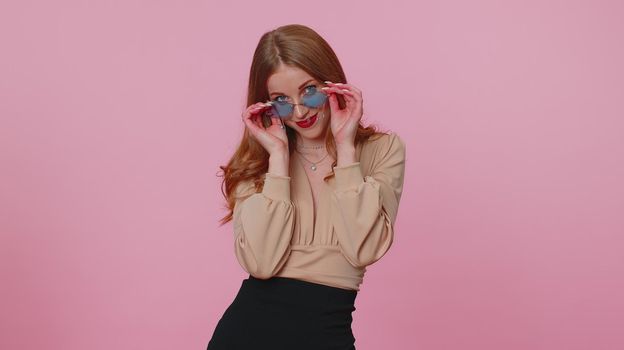Sincere cool cheerful casual businesswoman girl in beige blouse wearing red sunglasses, charming smile. People emotions concept. Young lovely adult woman posing isolated on pink studio wall background
