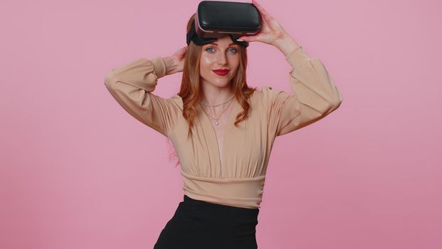 Teen brunette girl using virtual reality futuristic technology VR app headset helmet to play simulation 3D 360 video game, drawing. Young woman on pink studio background. People sincere emotions
