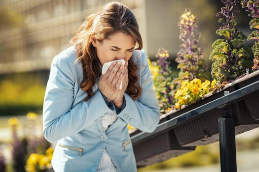 A young business woman blowing her nose out during a break outside due to allergies or colds.