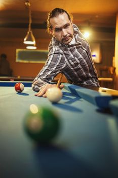 Concentrated middle aged man while playing billiards in billiard club after work.