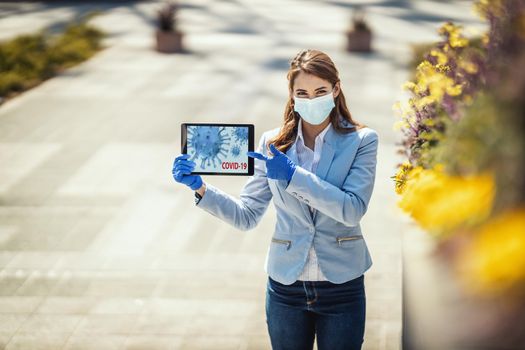 Young business woman with protective mask on their face is showing an animation of a corona virus on a tablet.