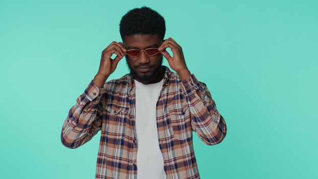 Portrait of one candid cheerful stylish african american man wearing sunglasses, charming smile. People emotions concept. Young lovely adult guy posing isolated alone on blue studio wall background