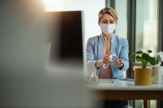 Business woman in a medical protective mask uses antibacterial antiseptic gel for hands disinfection and works from home at the computer during self-isolation and quarantine to avoid infection during flu virus outbreak and coronavirus epidemic .