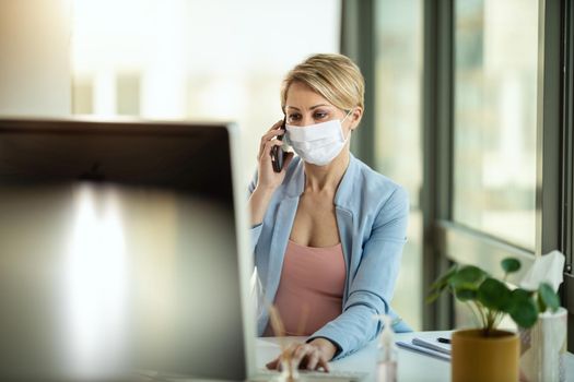Business woman in a medical protective mask talking on a smartphone and works at the computer during self-isolation and quarantine to avoid infection during flu virus outbreak and coronavirus epidemic.