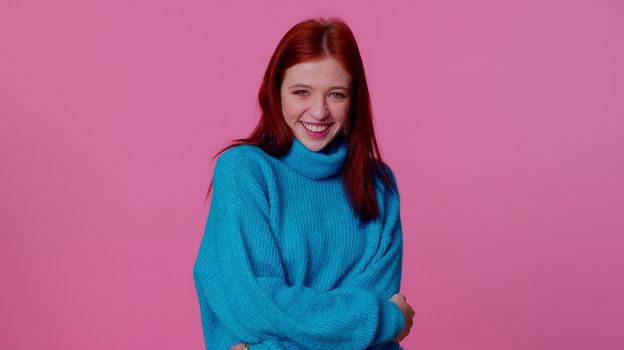 Cheerful beautiful teenager student girl in blue sweater smiling and looking at camera. Young fashion lovely model woman indoors studio shot isolated on pink wall background. Female nature beauty