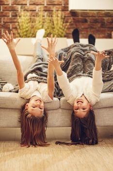 Portrait of two little girls laughing lying upside down, happy cheerful sisters having fun together on sofa at home covered with soft blanket.