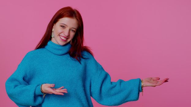 Pretty redhead teen girl showing thumbs up and pointing empty place, advertising area for commercial text, copy space for goods promotion. Young adult woman. Indoor studio shot on pink background