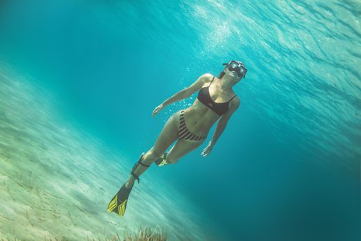 A beautiful young woman is having fun at summer vacation exploring seafloor during scuba diving in sea.