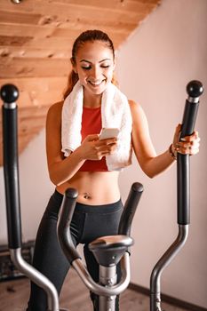 Beautiful young woman using smartphone while exercising on stepper at home.