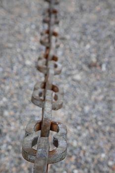 A light gray metal chain made of steel and showing its age is seen up close as it hangs above the broken stone ballast. Selective focus.Vertical view