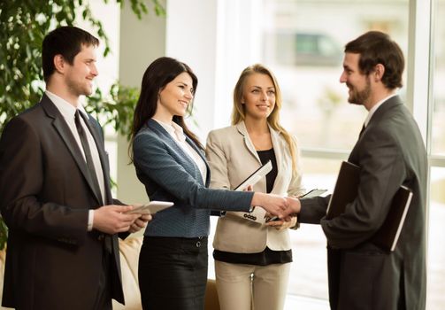 Group of business people congratulating their handshaking colleagues after signing contract
