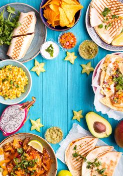 Traditional Mexican food background. Table with different Mexican dishes. Cheese nachos, tacos, guacamole, quesadilla, burrito, fajitas, tortilla chips, Mexican fruits. Tex-Mex cuisine. Space for text