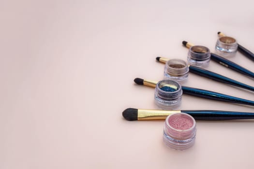 Composition with decorative makeup products golden brushes and colorful eye shadows on pastel pink background. photo