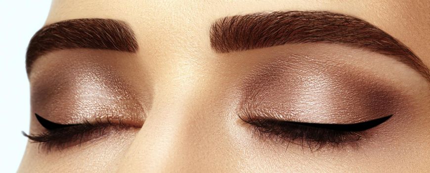 Beautiful macro shot of female eye with classic smoky makeup. Perfect shape of eyebrows, brown eyeshadows and long eyelashes. Cosmetics and make-up. Closeup macro shot of fashion smoky eyes visage