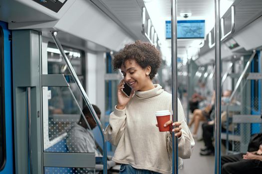 close-up. young woman with a takeaway coffee talking on a smartphone in a subway car .