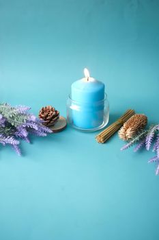 Natural candle in a glass jar and dried flowers on blue .