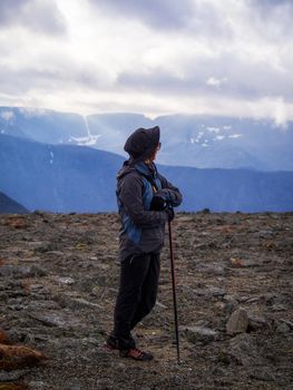 A woman in a hat on a mountain slope looks through binoculars in autumn against the backdrop of a lake and mountains. view from the back. photo