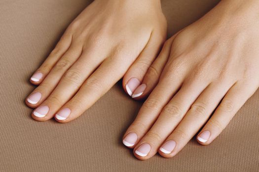 Young Female Palm on beige background. Beautiful Glamour Manicure. French Style. Nail polish. Care about Hands and Nails, clean Skin