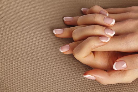 Young Female Palm on beige background. Beautiful Glamour Manicure. French Style. Nail polish. Care about Hands and Nails, clean Skin