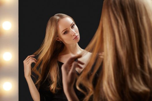 Portrait of beautiful young woman. She is looking to the makeup artrist mirror with bright lights. Glamour luxury look with perfect fashion make-up and blond shiny hair