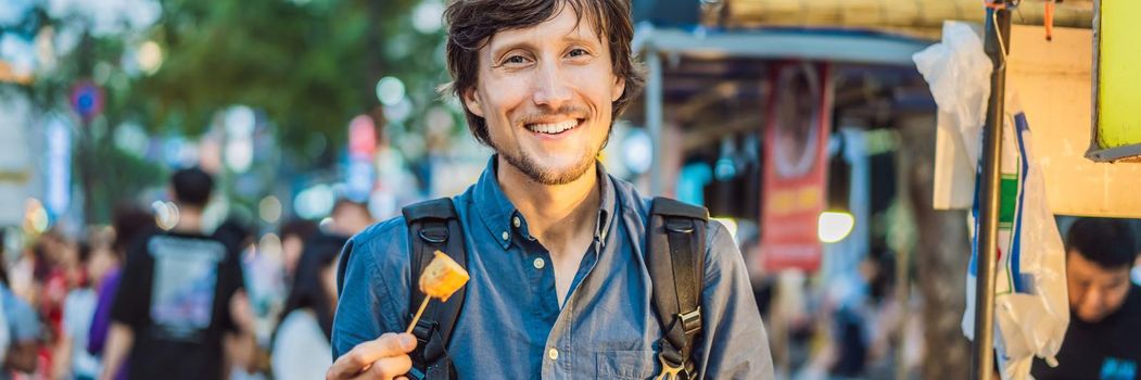 Young man tourist eating Typical Korean street food on a walking street of Seoul. Spicy fast food simply found at local Korean martket, Soul Korea. BANNER, LONG FORMAT