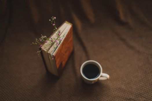 A book with flowers and cup of coffee on dark background top view.