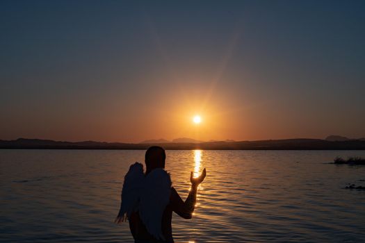 dark silhouette of a man with wings with warm orange color in the sky by sunlight. carnival costume wings High quality photo