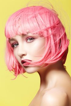 Young model in pink wig. Beautiful model with fashion makeup. Bright spring look. Sexy hair color, medium hairstyle on yellow background