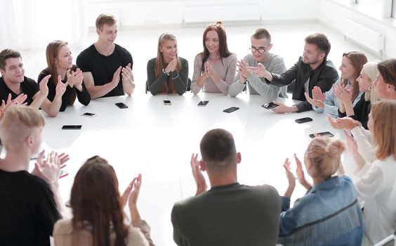 group of young people applauding, sitting at a round table . photo with copy space