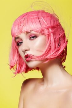 Young model in pink wig. Beautiful model with fashion makeup. Bright spring look. Sexy hair color, medium hairstyle on yellow background