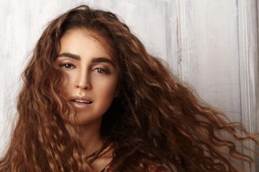 Beautiful young woman with long curly hairstyle, fashion jewelry with long brunette hair. Sexy girl in vogue style. Pretty arabian beauty portrait of female face. Indian style clothes, long dress