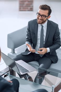 Young businessman sitting comfortably in an open modern office, smiling while having a positive conversation with a coworker