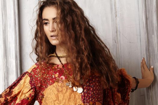 Beautiful young woman with long curly hairstyle, fashion jewelry with long brunette hair. Sexy girl in vogue style. Pretty arabian beauty portrait of female face. Indian style clothes, long dress