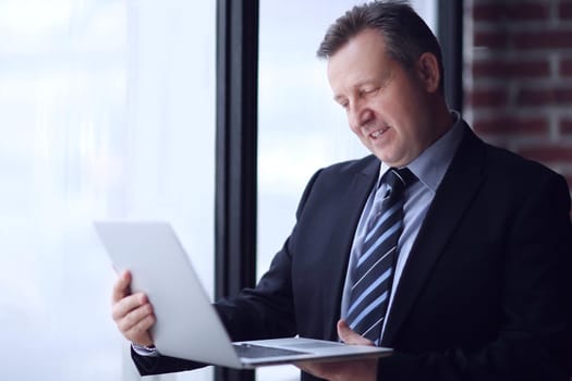 confident businessman with laptop standing in office.photo with copy space