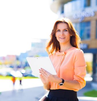Portrait of pretty businesswoman in smart casual using digital tablet outdoors