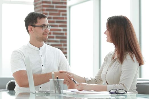 businessman and businesswoman shaking hands while sitting at the Desk. concept of cooperation