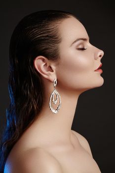 Beautiful woman in luxury fashion earrings. Diamond shiny jewelry with brilliants. Sexy retro style portrait. Model with glamour accessories jewelery, fashion makeup, clean shiny skin and wet hair