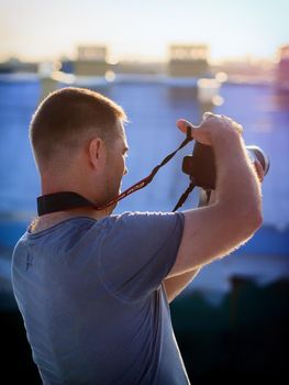 A photographer is standing on the roof of the house and photographs the city landscape.