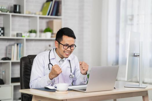 Asian doctor man happy congrats and working with laptop computer. Male doctor work at home office hospital. Health hospital concept