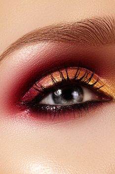 Closeup female eye with fashion bright make-up. Beautiful gold, red eyeshadow, wet glitter, black eyeliner. Perfect Shape of Eyebrows