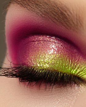 Closeup female eye with beautiful fashion bright make-up. Beautiful shiny gold, pink eyeshadow, wet glitter, black eyeliner